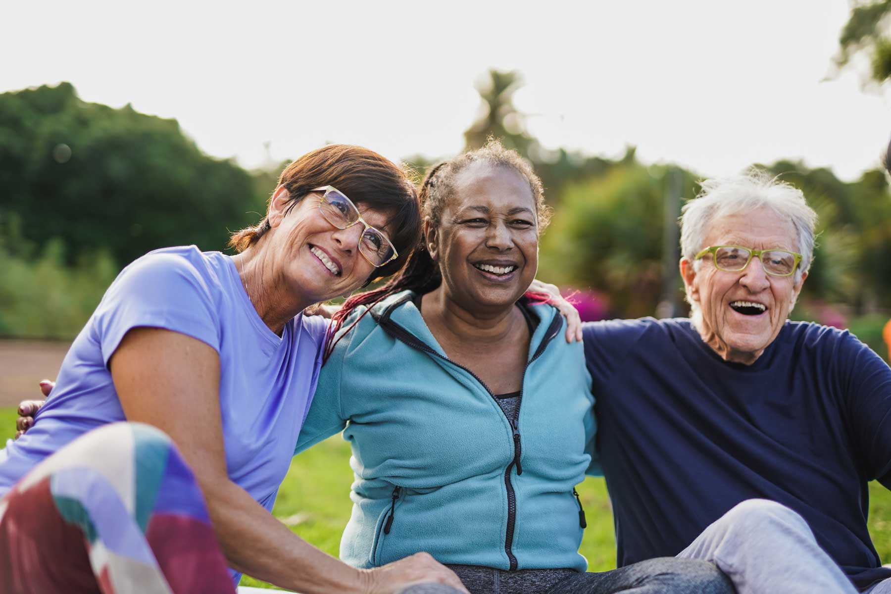 a group of senior friends sitting outside with their arms around each other