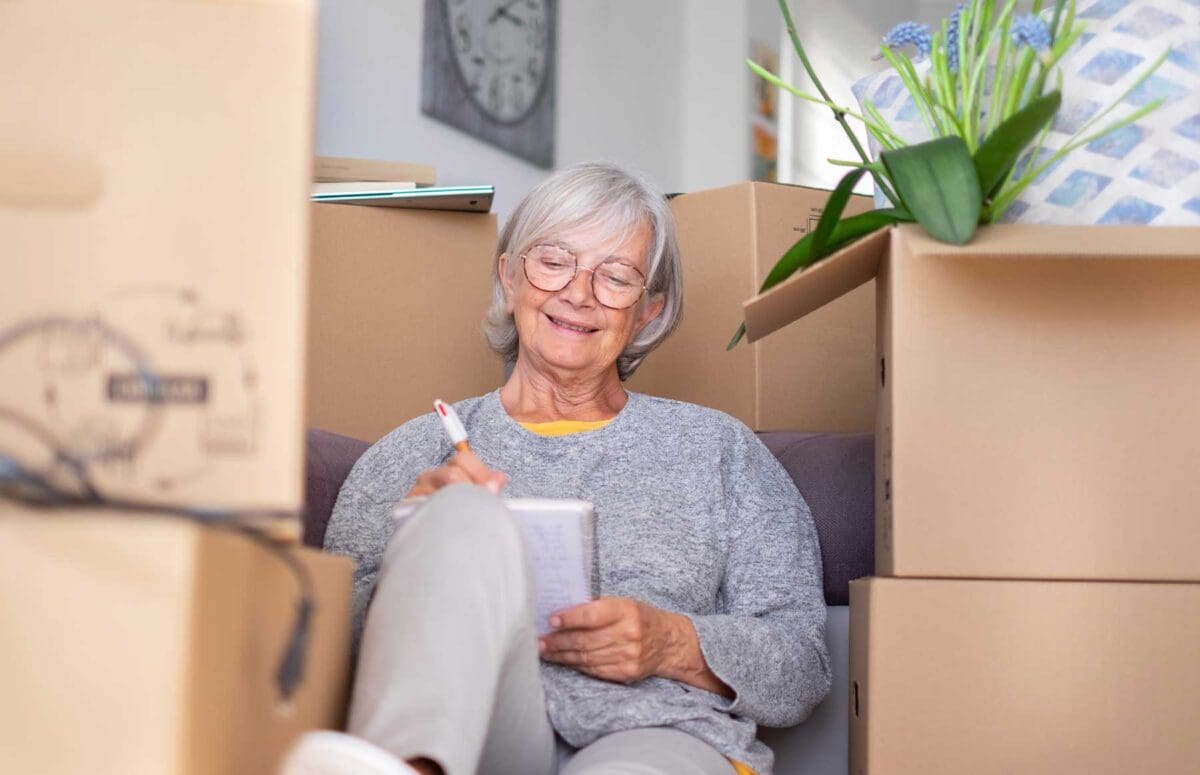 senior woman checking her moving list as she sits around her moving boxes