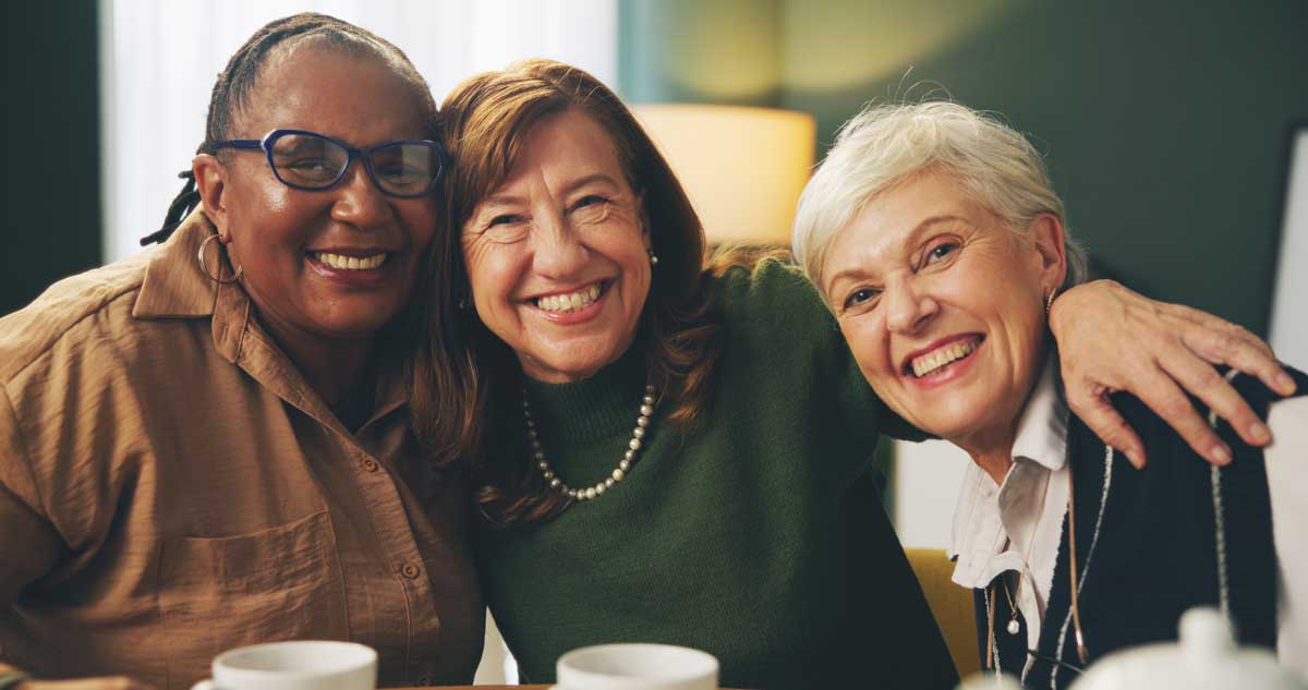 three senior woman smiling with their arms around each other as they pose for a picture